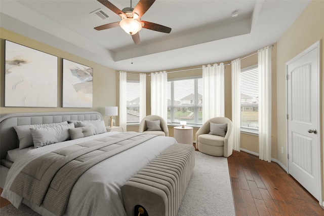 bedroom with baseboards, visible vents, a ceiling fan, wood finished floors, and a tray ceiling