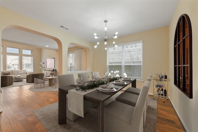 dining room with baseboards, visible vents, arched walkways, wood finished floors, and a notable chandelier