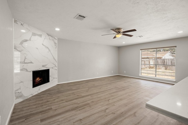 unfurnished living room featuring a textured ceiling, wood finished floors, a high end fireplace, and visible vents