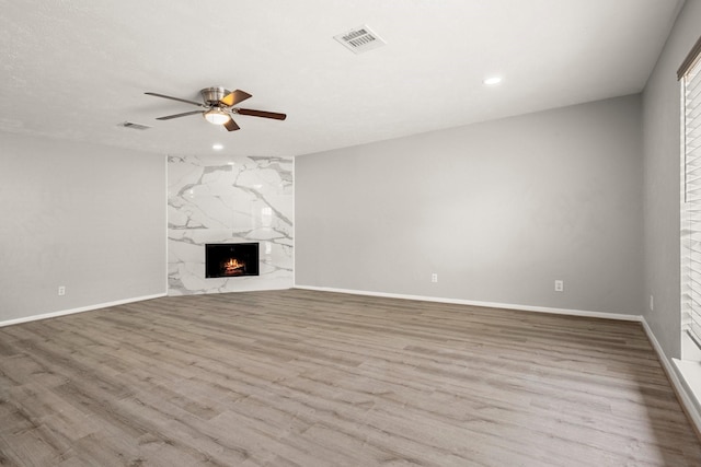 unfurnished living room featuring light wood-style floors, ceiling fan, visible vents, and a high end fireplace