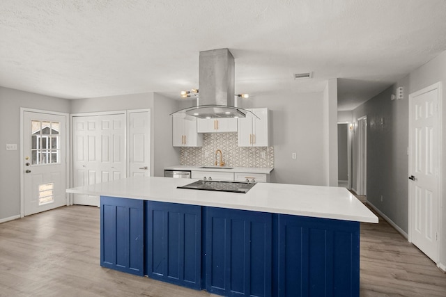 kitchen featuring light countertops, island range hood, a sink, and white cabinets