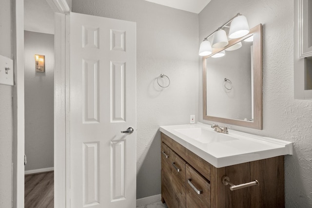 bathroom with a textured wall, vanity, and baseboards