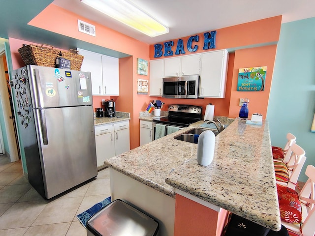 kitchen featuring stainless steel appliances, visible vents, a sink, light stone countertops, and a peninsula