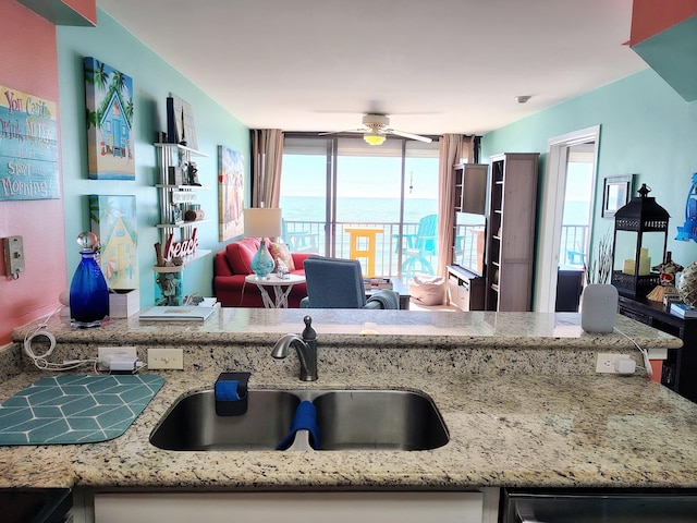 kitchen with light stone counters, a ceiling fan, open floor plan, and a sink