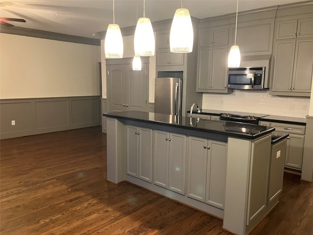 kitchen featuring appliances with stainless steel finishes, dark countertops, pendant lighting, and a kitchen island with sink