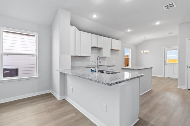 kitchen featuring white cabinets, a peninsula, light wood-style floors, pendant lighting, and a sink