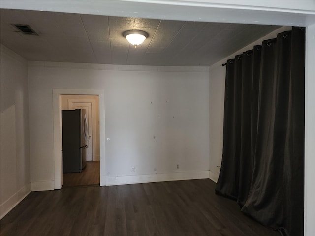 unfurnished room with dark wood-style flooring, visible vents, and baseboards