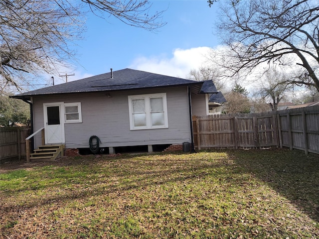 back of house featuring entry steps, a fenced backyard, a shingled roof, and a lawn