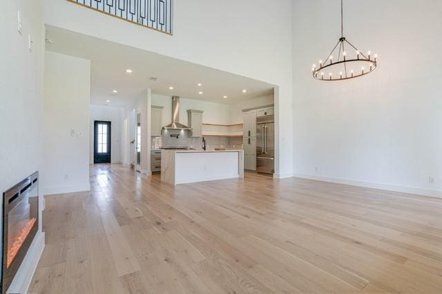 unfurnished living room with baseboards, a high ceiling, a sink, a chandelier, and light wood-style floors