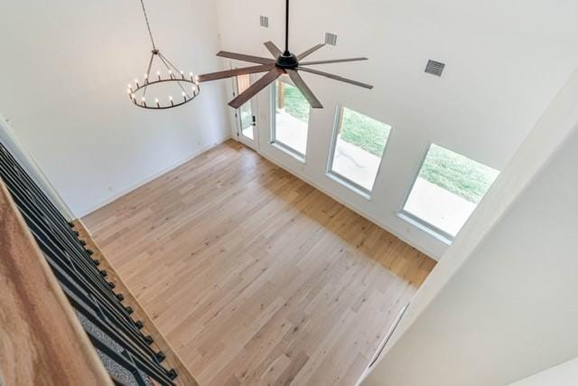 unfurnished living room with ceiling fan with notable chandelier, light wood finished floors, a towering ceiling, and visible vents