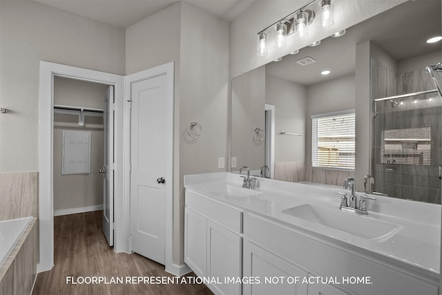 bathroom with tiled shower, a sink, visible vents, and wood finished floors