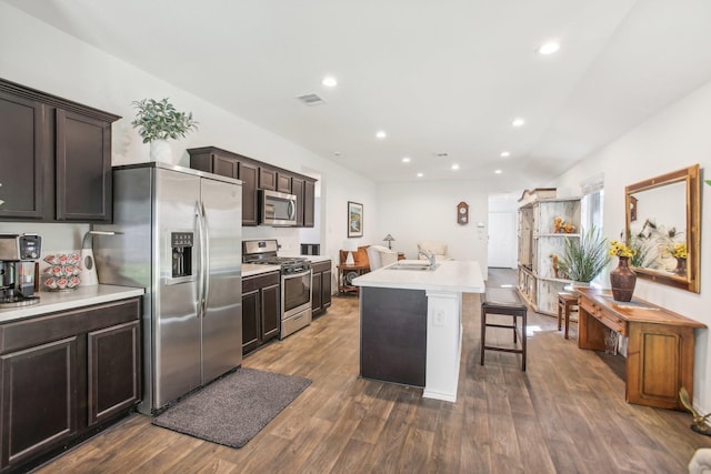 kitchen featuring dark wood-style flooring, a breakfast bar area, stainless steel appliances, light countertops, and an island with sink