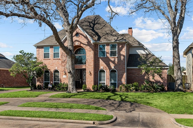 view of front facade with brick siding, a chimney, roof with shingles, fence, and a front yard