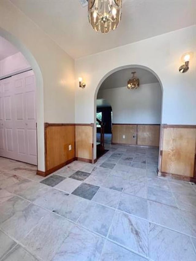 unfurnished room featuring a wainscoted wall, arched walkways, and an inviting chandelier