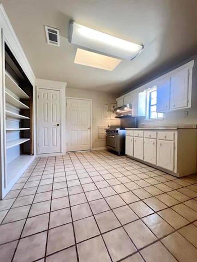 kitchen with light tile patterned floors, light countertops, stainless steel range, and white cabinets