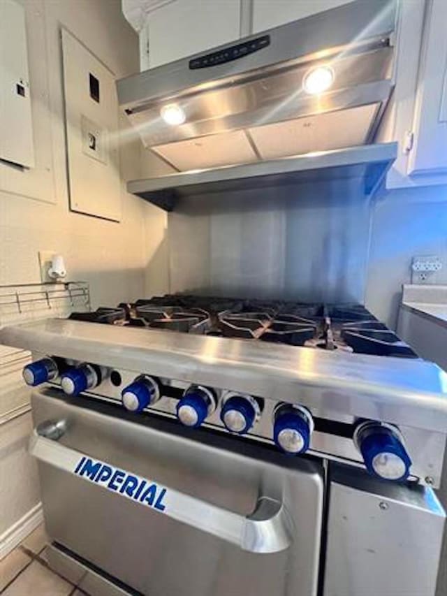 kitchen featuring light tile patterned floors, under cabinet range hood, white cabinetry, light countertops, and stainless steel range with gas stovetop