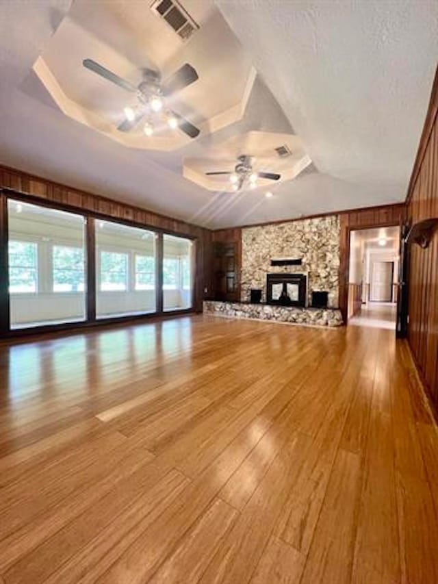 unfurnished living room with light wood finished floors, wooden walls, visible vents, ceiling fan, and a stone fireplace