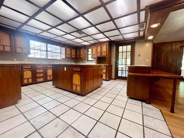 kitchen featuring brown cabinetry, a center island, visible vents, and coffered ceiling