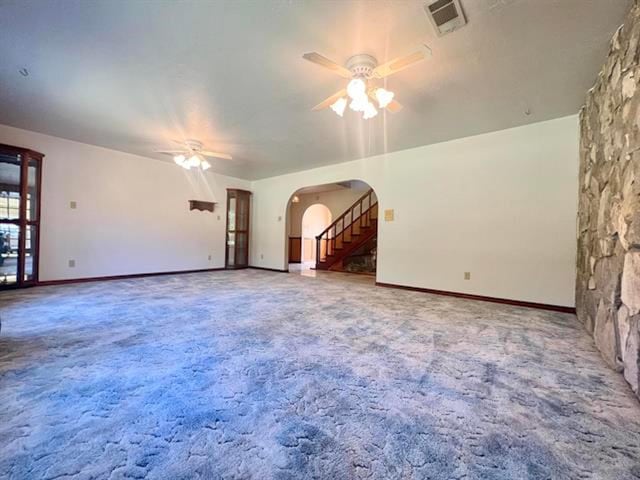 unfurnished living room featuring visible vents, arched walkways, ceiling fan, carpet, and stairs