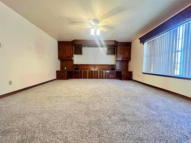 unfurnished living room featuring ceiling fan, baseboards, a textured ceiling, and carpet flooring