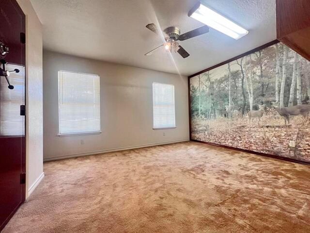 unfurnished room featuring a ceiling fan, light carpet, vaulted ceiling, a textured ceiling, and baseboards