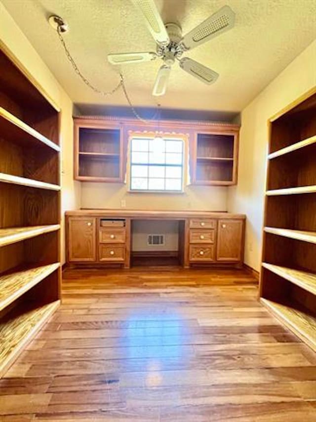 unfurnished office with visible vents, a ceiling fan, light wood-style flooring, a textured ceiling, and built in desk