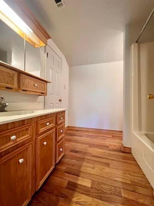 kitchen with lofted ceiling, visible vents, light countertops, light wood-style flooring, and brown cabinetry