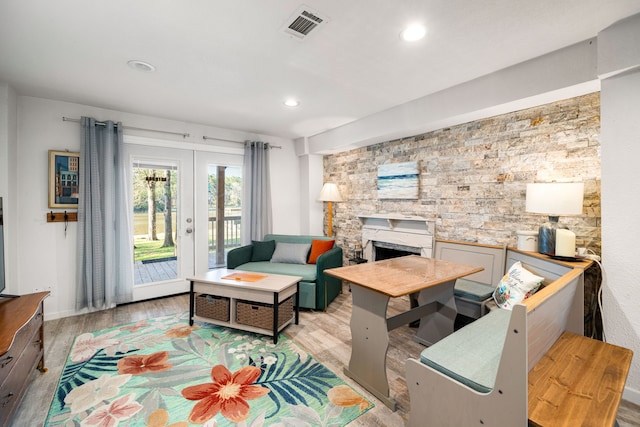 living room featuring a stone fireplace, light wood-style flooring, recessed lighting, visible vents, and french doors