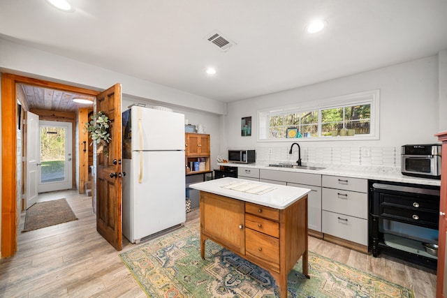 kitchen featuring light countertops, stainless steel microwave, visible vents, freestanding refrigerator, and a sink