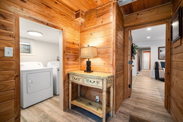 clothes washing area with laundry area, visible vents, washer and dryer, wood walls, and light wood-style floors