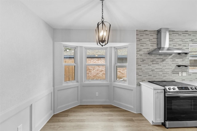 kitchen featuring white cabinets, stainless steel electric range oven, light countertops, wall chimney range hood, and pendant lighting