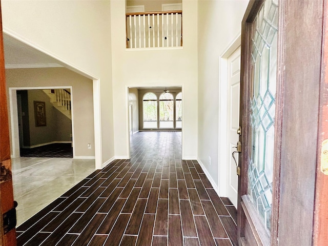 foyer entrance featuring wood tiled floor, crown molding, a towering ceiling, and baseboards