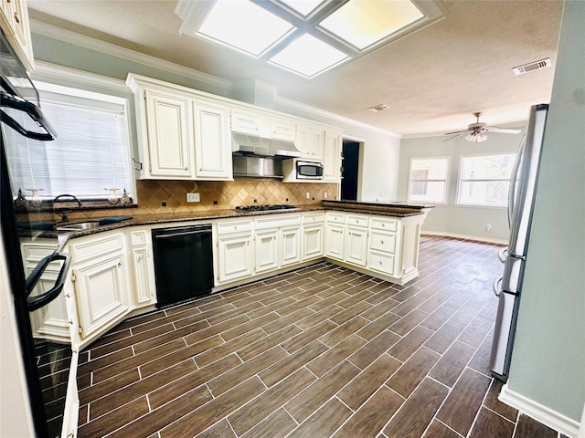 kitchen with a peninsula, visible vents, appliances with stainless steel finishes, range hood, and tasteful backsplash