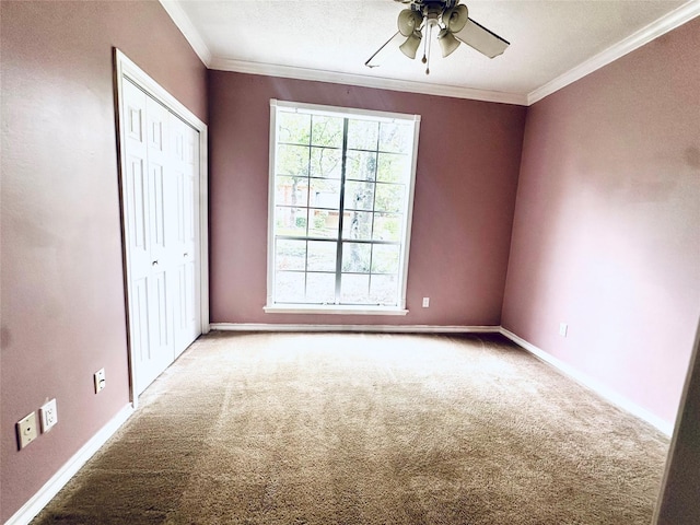 carpeted spare room featuring ornamental molding, ceiling fan, and baseboards