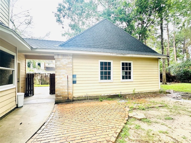 view of property exterior featuring a shingled roof, fence, and a patio