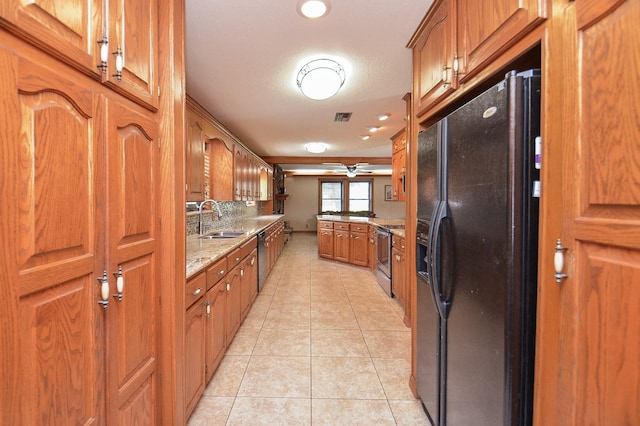 kitchen with appliances with stainless steel finishes, light tile patterned flooring, a sink, and brown cabinets