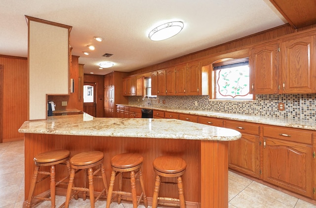 kitchen featuring a peninsula, a breakfast bar, brown cabinets, dishwasher, and tasteful backsplash