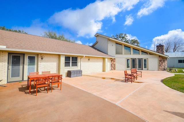 back of property featuring a shingled roof, a patio area, brick siding, and a chimney