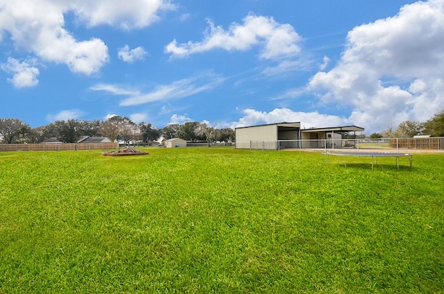 view of yard with a trampoline, an outdoor structure, and fence