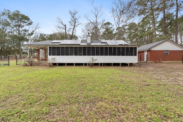 back of house featuring a yard, a chimney, a sunroom, and roof mounted solar panels