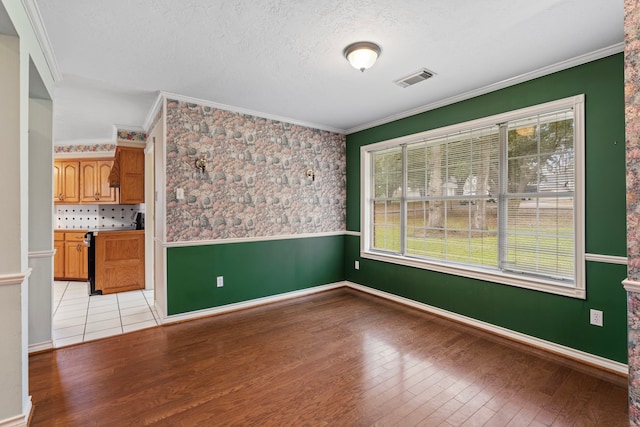 spare room with crown molding, visible vents, light wood-style flooring, wainscoting, and a textured ceiling