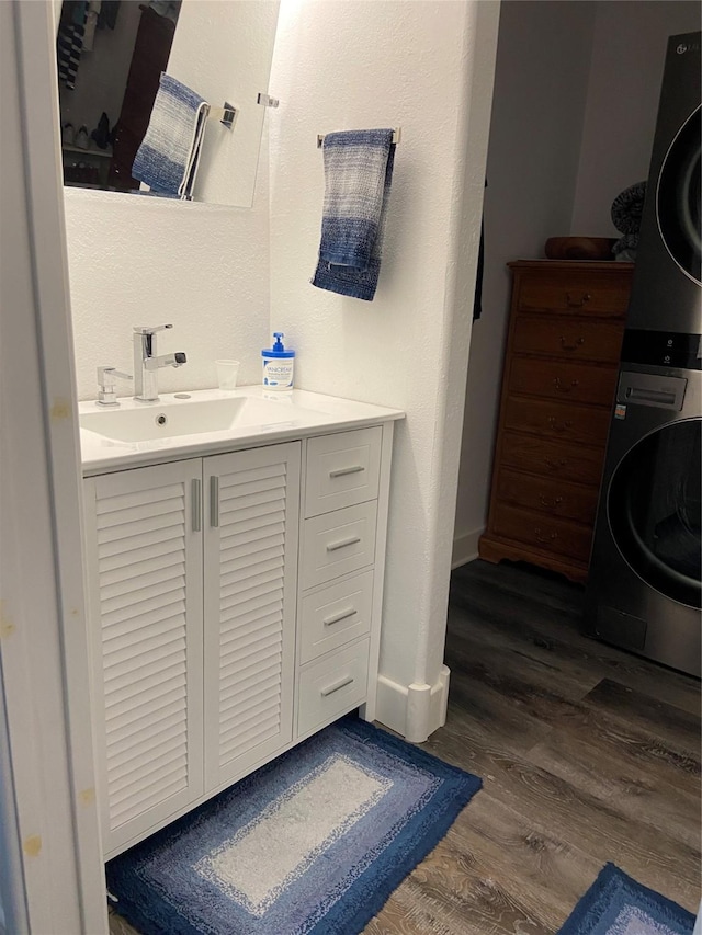 bathroom featuring stacked washer and dryer, vanity, baseboards, and wood finished floors