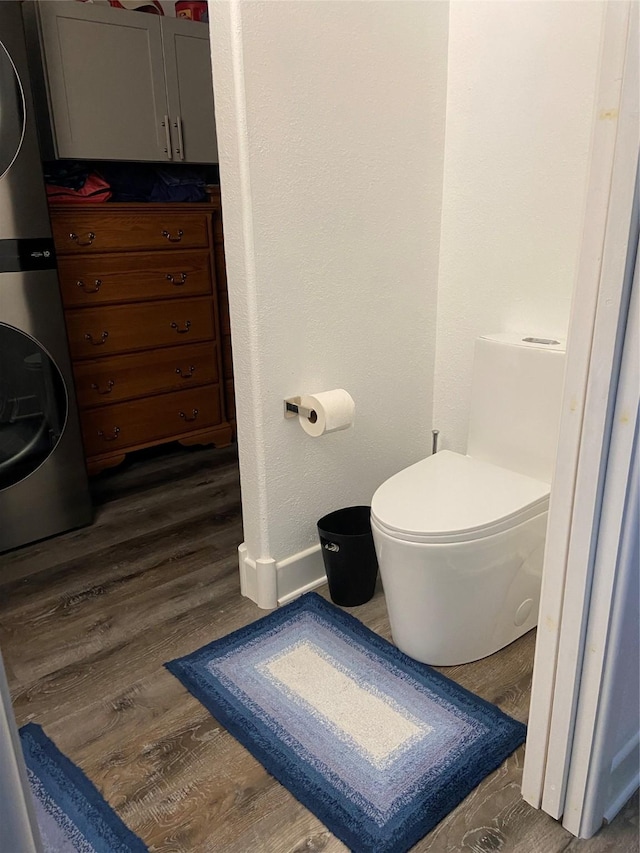 bathroom featuring toilet, stacked washing maching and dryer, and wood finished floors