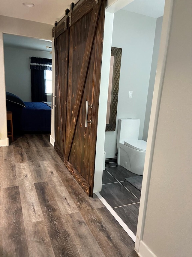 hall featuring a barn door, baseboards, and dark wood-style flooring