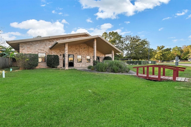 rear view of house with brick siding, a lawn, and fence