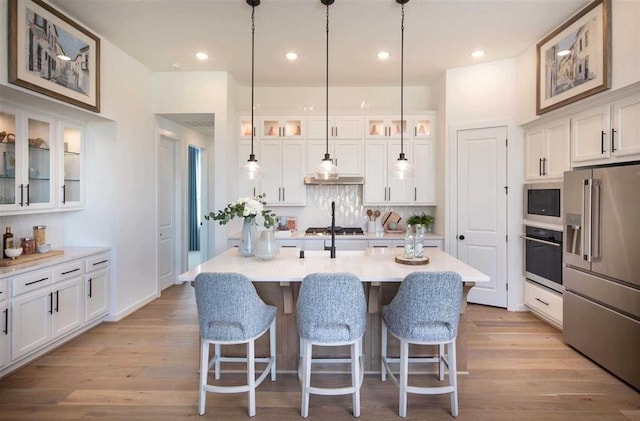 kitchen with a kitchen island with sink, glass insert cabinets, stainless steel appliances, and light countertops