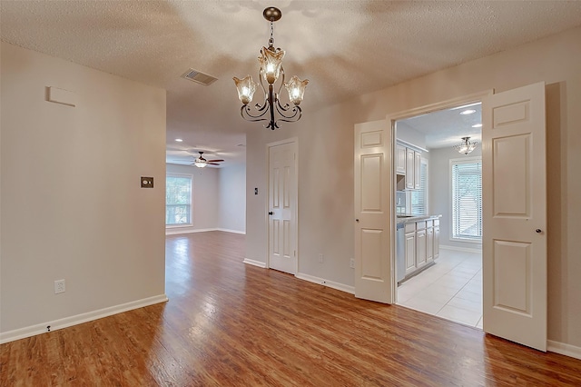 spare room featuring a textured ceiling, ceiling fan with notable chandelier, visible vents, baseboards, and light wood-type flooring