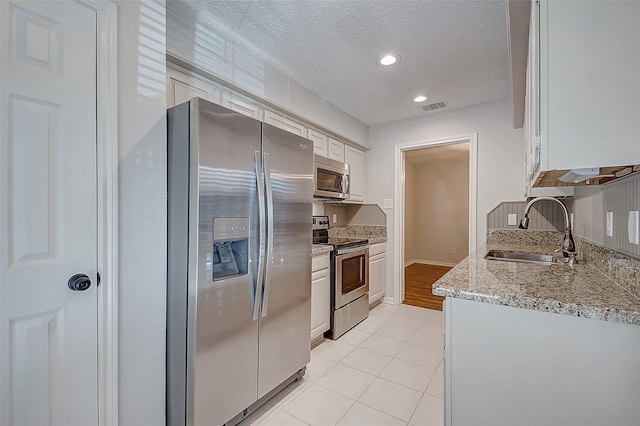 kitchen with visible vents, appliances with stainless steel finishes, white cabinets, a sink, and a textured ceiling