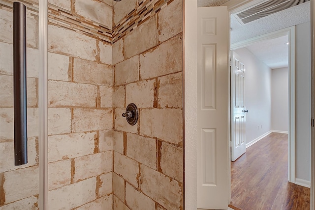 room details with wood finished floors, a tile shower, visible vents, and baseboards