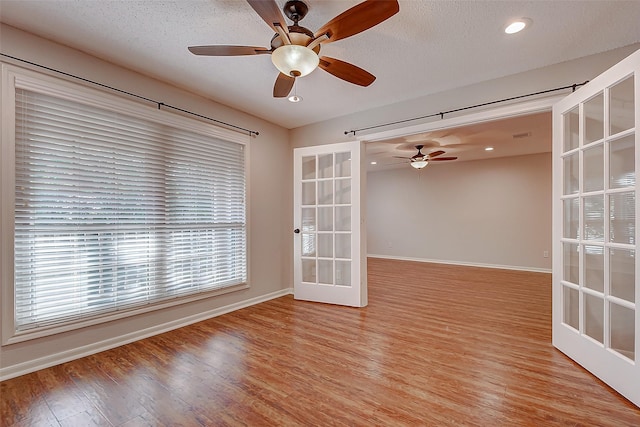 empty room featuring french doors, light wood-style floors, ceiling fan, a textured ceiling, and baseboards